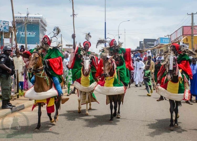Ceremonial horsemen and drummers fill an Ilorin street during a Durbar celebration, watched on by residents.