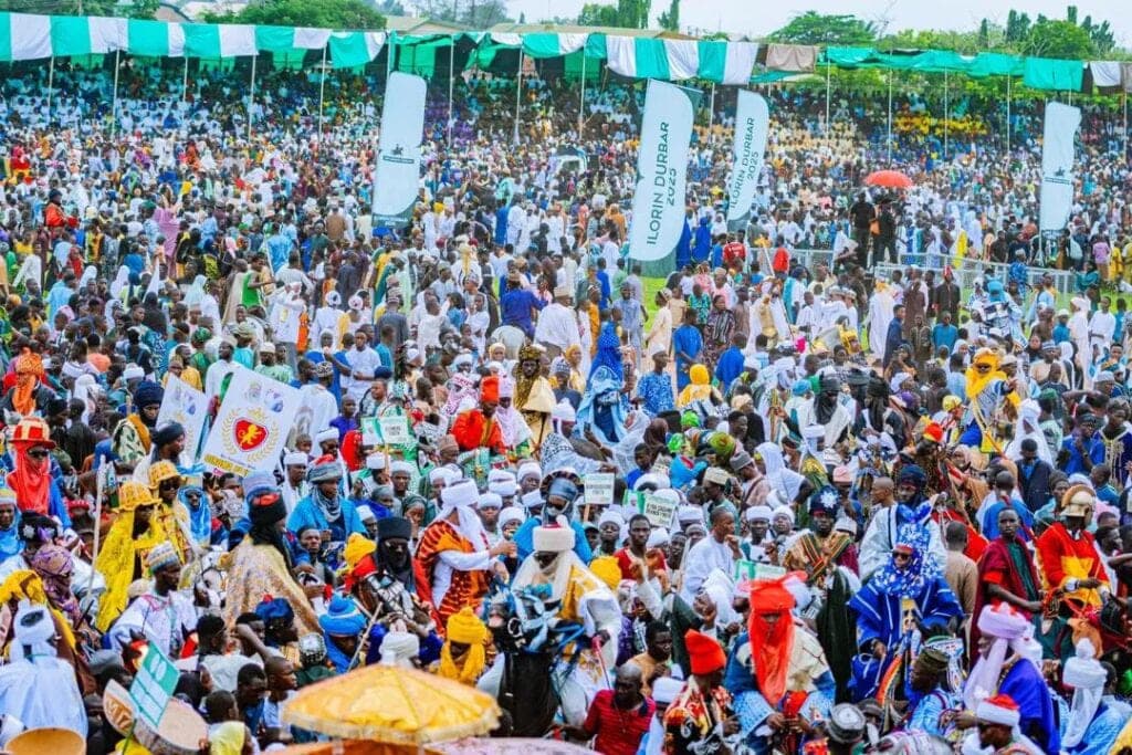 Thousands of residents in bright ceremonial dress fill the grounds of the Ilorin Durbar, banners rising above the crowd.